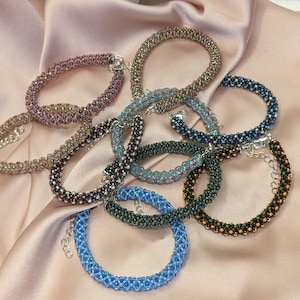 May include: A collection of eight beaded bracelets in various colors, including brown, black, blue, and green. The bracelets are made with small, round beads and have silver clasps.