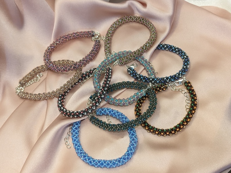 May include: A collection of eight beaded bracelets in various colors, including brown, black, blue, and green. The bracelets are made with small, round beads and have silver clasps.