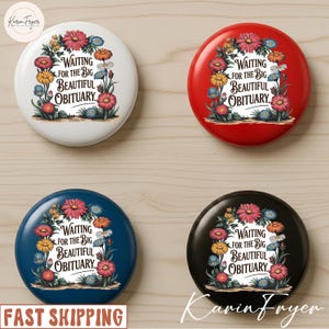 以下が含まれることがあります： 白、赤、ネイビーブルー、黒の4つの丸いボタン。それぞれに花のリースデザインと「Waiting for the Big Beautiful Obituary」の文字が描かれています。ボタンは明るい木材の表面にあります。