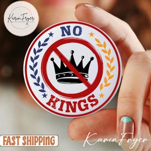 May include: A round white button with the words "NO KINGS" in red, with a black crown crossed out by a red circle. The button is decorated with blue and yellow accents and stars.