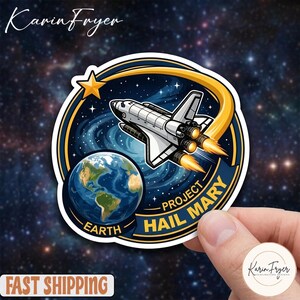 May include: A circular sticker featuring a space shuttle, Earth, and a star against a starry background. The text reads "PROJECT HAIL MARY" and "EARTH". The sticker has a blue, yellow, and white color scheme.