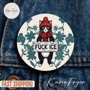 May include: A round button featuring a black and white cat wearing a red hat and scarf, holding a sign that reads "FUCK ICE." The cat is set against a cream background with teal floral accents.