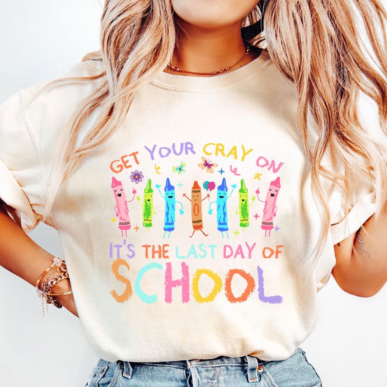 May include: Cream-colored sweatshirt with the text "Get Your Cray On" and "It's The Last Day Of School" in colorful letters. The design features cartoon crayons with smiling faces and arms raised in celebration.