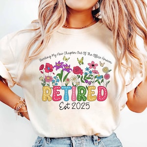 Puede incluir: Una camiseta blanca con un dise&ntilde;o floral colorido y el texto "Starting My New Chapter Out Of The Office Forever RETIRED Est 2025".