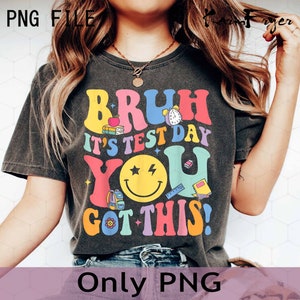 May include: A dark grey t-shirt with a colorful graphic that says "Bruh it's test day you got this!" The graphic includes a smiley face with stars, a clock, books, and a pencil.