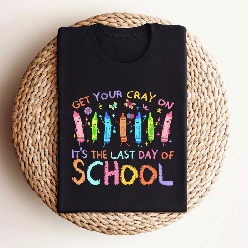 May include: Black t-shirt with a colorful crayon graphic and the text "GET YOUR CRAY ON IT'S THE LAST DAY OF SCHOOL". The design features smiling crayons in various colors, perfect for back-to-school or end-of-year celebrations.
