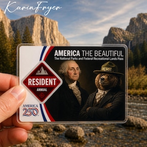 May include: A clear plastic America the Beautiful National Parks Pass. The pass features an image of George Washington and a bear wearing a hat that says "RESIST." The pass also includes the text "RESIDENT ANNUAL" and "AMERICA 250."