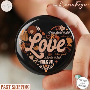 Puede incluir: Un soporte redondo negro para teléfono con un diseño en forma de corazón. El diseño incluye la palabra "Love" en fuente marrón, junto con la cita "I have decided to stick with love is too great a burden to bear - MLK JR."