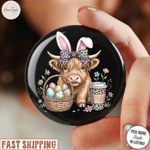Puede incluir: Un soporte redondo negro para teléfono con una vaca de las Tierras Altas con orejas de conejo y un lazo, sosteniendo una cesta de huevos de Pascua y una taza de café. El diseño incluye flores coloridas y un estampado de leopardo.