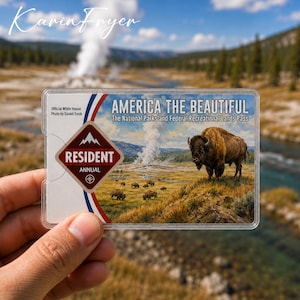 May include: An America the Beautiful National Parks and Federal Recreational Lands Pass card in a clear plastic holder. The card features a brown bison in a grassy landscape with a geyser, text reading America the Beautiful, and a Resident Annual badge.