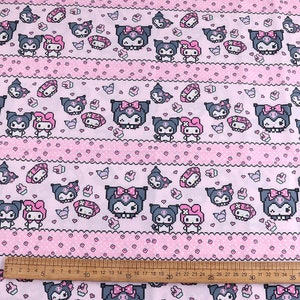 Op de afbeelding: Roze en witte stof met een herhalend patroon van zwart-witte cartoonfiguren. De figuren zijn in een gepixelde stijl en bevatten een kat met een strik en een konijn met een strik. De stof heeft een roze en witte stippenachtergrond met een roze en witte gestreepte rand.