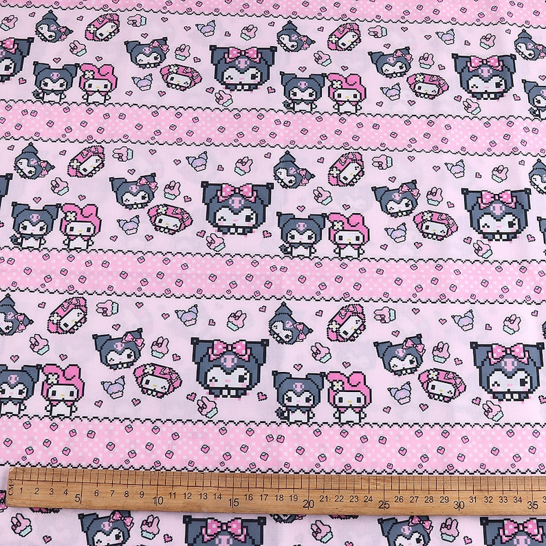 Op de afbeelding: Roze en witte stof met een herhalend patroon van zwart-witte cartoonfiguren. De figuren zijn in een gepixelde stijl en bevatten een kat met een strik en een konijn met een strik. De stof heeft een roze en witte stippenachtergrond met een roze en witte gestreepte rand.