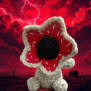 May include: A crocheted Demogorgon plushie with a white body, red and white petal-like head, and a black center. The background features a red sky with lightning and a desolate landscape, evoking a sense of mystery and fantasy.
