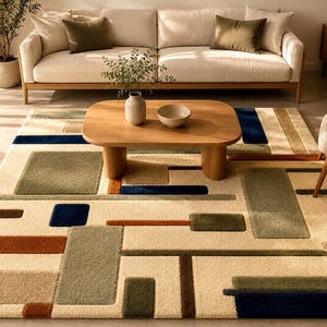 May include: A cream-coloured geometric rug featuring rectangular shapes in green, brown, and blue. A wooden coffee table and a beige sofa are in the background, creating a cosy living room setting. The rug's design adds a modern touch.
