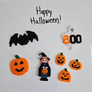 May include: A set of plastic canvas needlepoint decorations featuring the text Happy Halloween! above a black bat, a white ghost with the word BOO, a large orange pumpkin, a witch figure, and three small orange pumpkins with black faces.