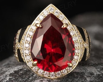 May include: A pear-shaped red gemstone ring with a gold band and a halo of smaller white gemstones.