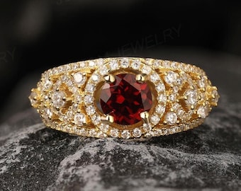 May include: A gold ring featuring a large red gemstone encircled by smaller white gemstones. The ring is displayed against a dark grey backdrop.