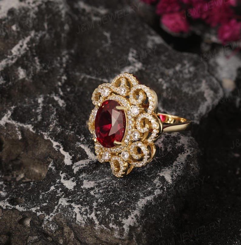 May include: A gold ring featuring a large oval ruby gemstone surrounded by smaller diamonds. The ring has a delicate, floral design.