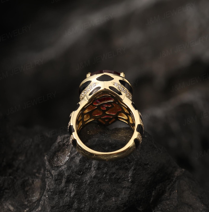 May include: A gold ring featuring a large red gemstone surrounded by smaller white gemstones. The ring has a black and gold patterned band.