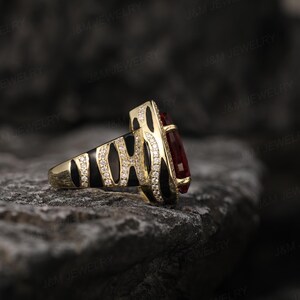 May include: A gold ring featuring a black and white zebra print design and a large red gemstone. The ring is displayed against a dark grey background.