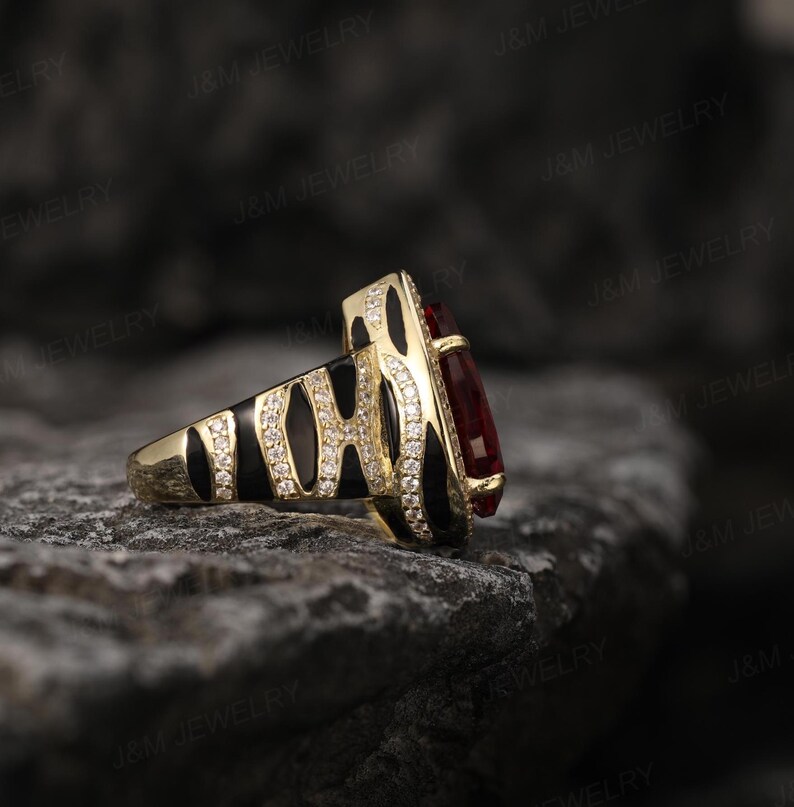 May include: A gold ring featuring a black and white zebra print design and a large red gemstone. The ring is displayed against a dark grey background.