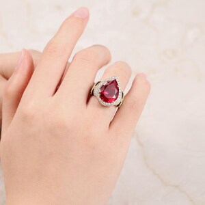 May include: A gold ring featuring a large pear-shaped red gemstone surrounded by smaller clear gemstones.