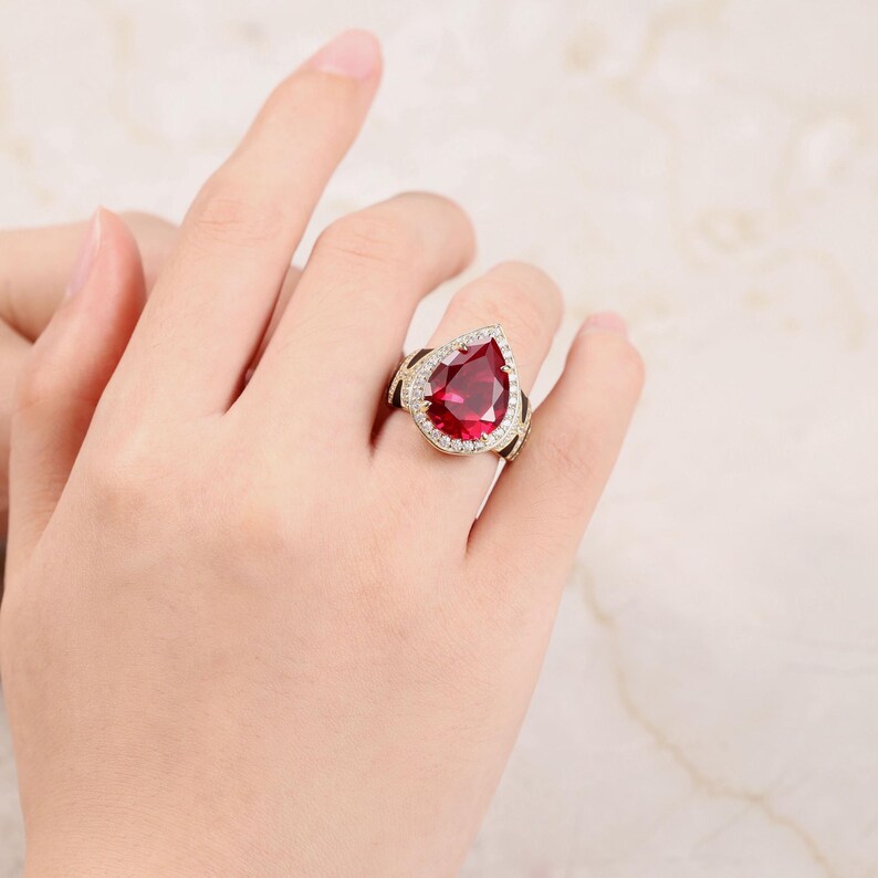 May include: A gold ring featuring a large pear-shaped red gemstone surrounded by smaller clear gemstones.