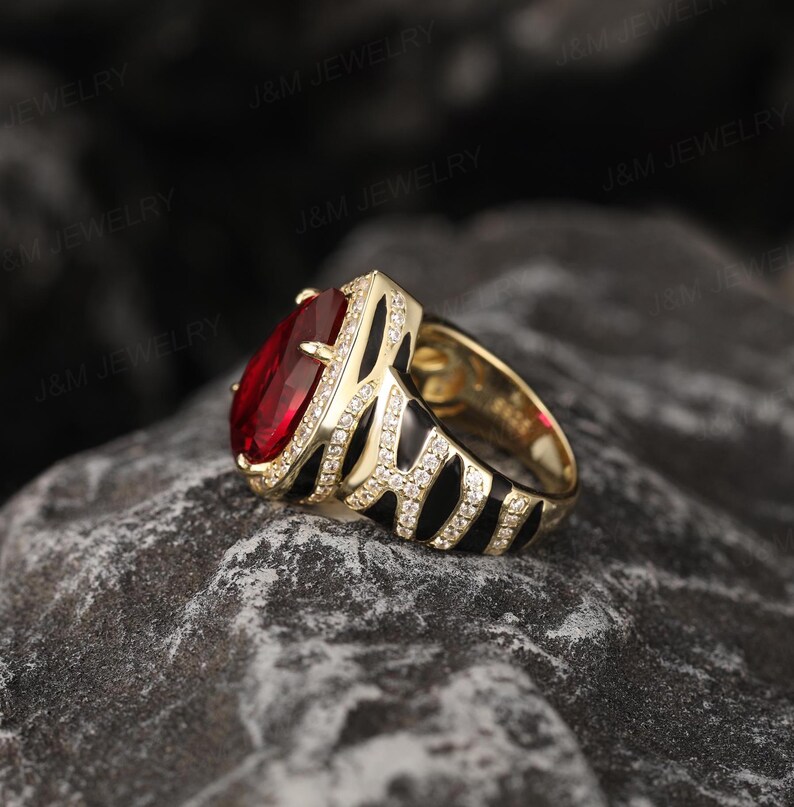 May include: A gold ring featuring a large red gemstone and a black and white zebra print band. The ring is set with small clear stones.