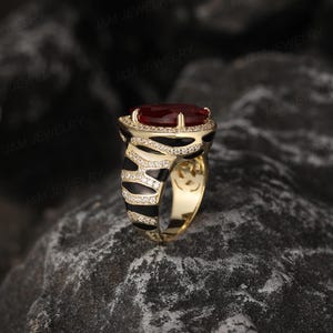 May include: A gold ring featuring a large red gemstone set in a black and white zebra print band.