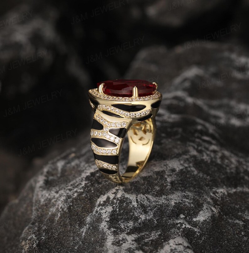 May include: A gold ring featuring a large red gemstone set in a black and white zebra print band.