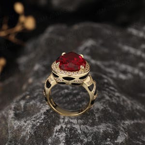 May include: A gold ring featuring a large red heart-shaped gemstone encircled by smaller clear gemstones. The band of the ring is black with a white pattern.