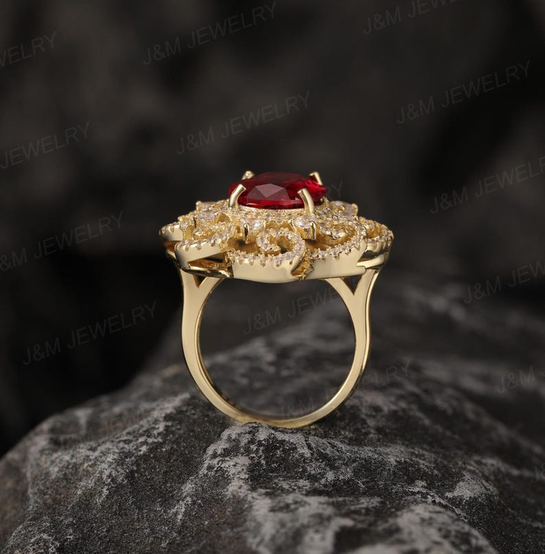 May include: A gold ring featuring a large red gemstone surrounded by smaller white gemstones. The ring has a floral design.