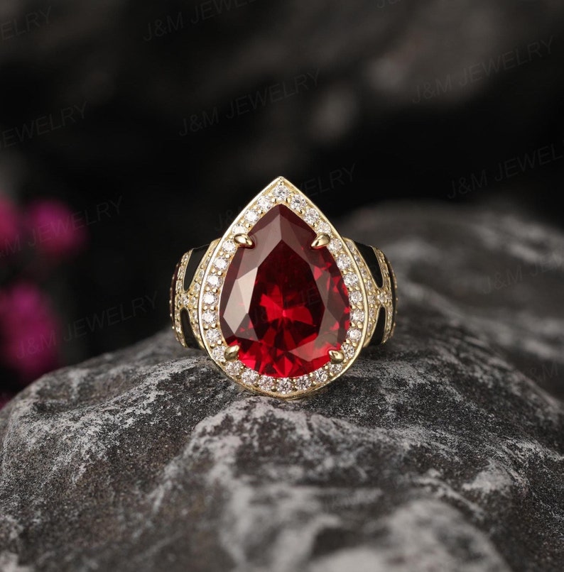 May include: A pear-shaped red gemstone ring with a gold band and a halo of smaller white gemstones.