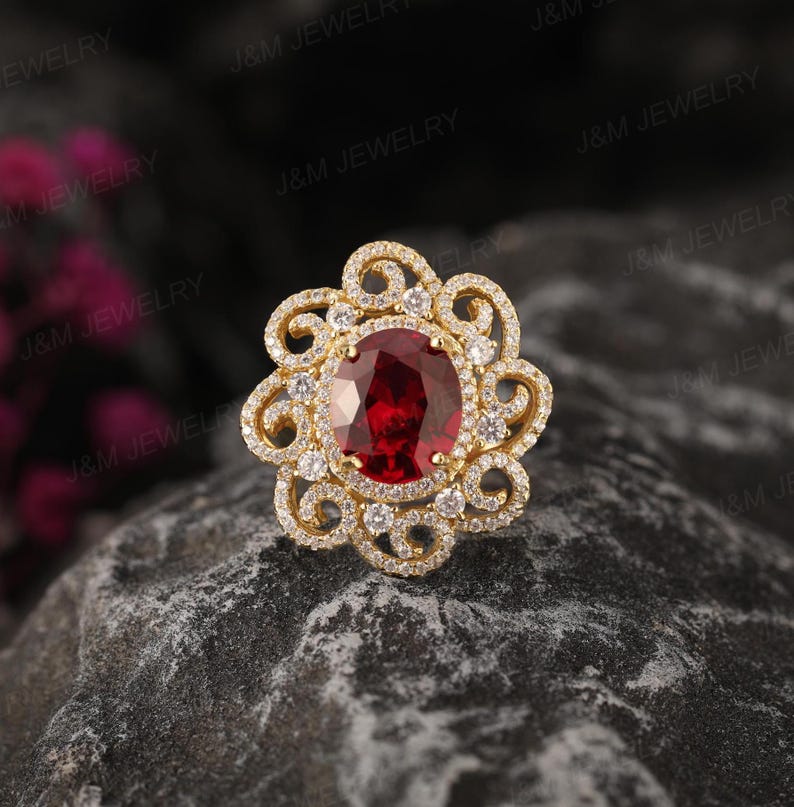 May include: A gold ring featuring a large red gemstone encircled by smaller white gemstones. The ring has a floral design.