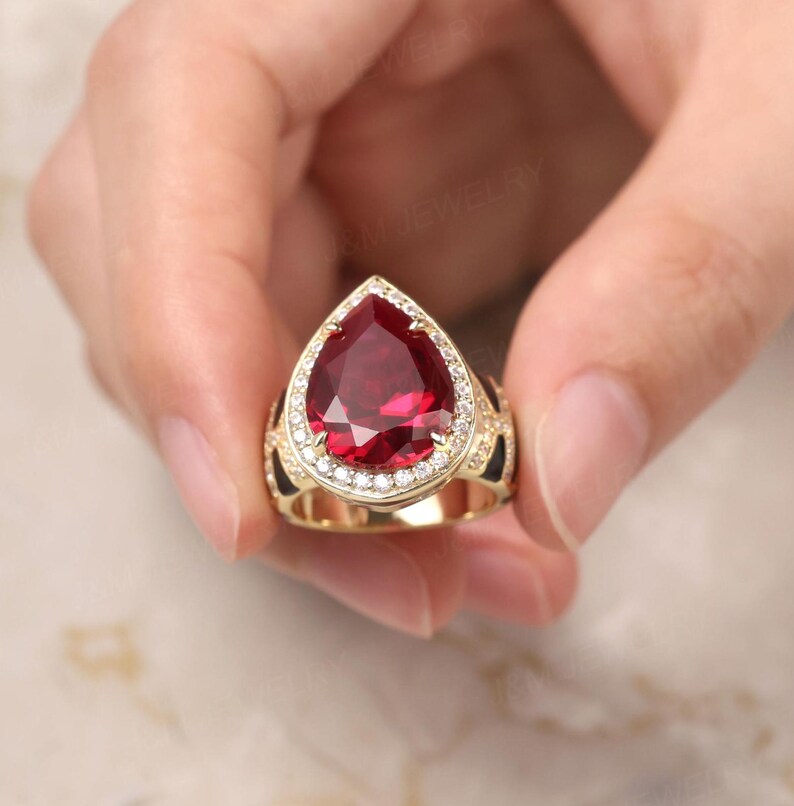 May include: A gold ring featuring a large pear-shaped red gemstone encircled by a halo of smaller white gemstones.