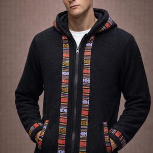 May include: A black fleece zip-up hoodie featuring a full-length front zipper and a hood. The garment is accented with vertical bands of colorful, multi-patterned woven fabric along the zipper, hood edge, sleeve cuffs, pockets, and hem.