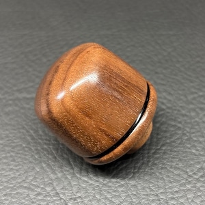May include: A small, rounded, polished wooden object with a smooth, light brown grain pattern. The object features a distinct horizontal seam separating the top section from the base, creating a two-part structure with a glossy, reflective finish.