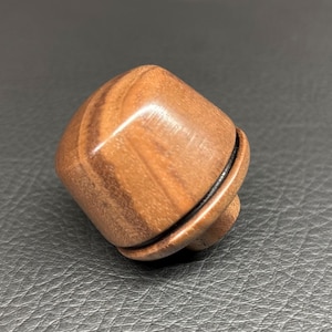 May include: A polished brown wooden knob with a smooth, rounded square shape and visible natural wood grain patterns. The knob features a distinct horizontal groove near the base, separating the main body from a smaller, cylindrical attachment point.
