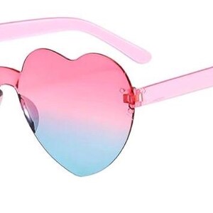 May include: Heart-shaped sunglasses featuring a rimless design with a gradient color transition from pink at the top to light blue at the bottom. The temples are made of translucent pink plastic, and the lenses are connected by a central bridge.
