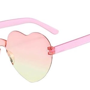 May include: Rimless heart-shaped sunglasses featuring a gradient lens transition from a soft pink at the top to a pale yellow at the bottom. The frames include translucent pink plastic temples attached to the lenses with small metal hinges.