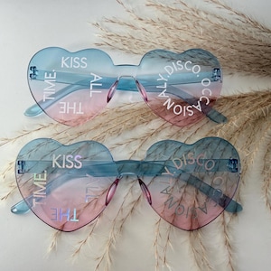 May include: Two pairs of heart-shaped sunglasses with a blue to pink gradient tint. The lenses feature white text printed in a circular pattern that reads KISS THE TIME ALL DISCO OCCASIONALLY. The frames are rimless with matching blue temples.