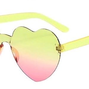 May include: Heart-shaped sunglasses featuring a rimless design with a gradient lens transition from yellow at the top to pink at the bottom. The frames include translucent yellow plastic temples and a matching yellow bridge connecting the lenses.