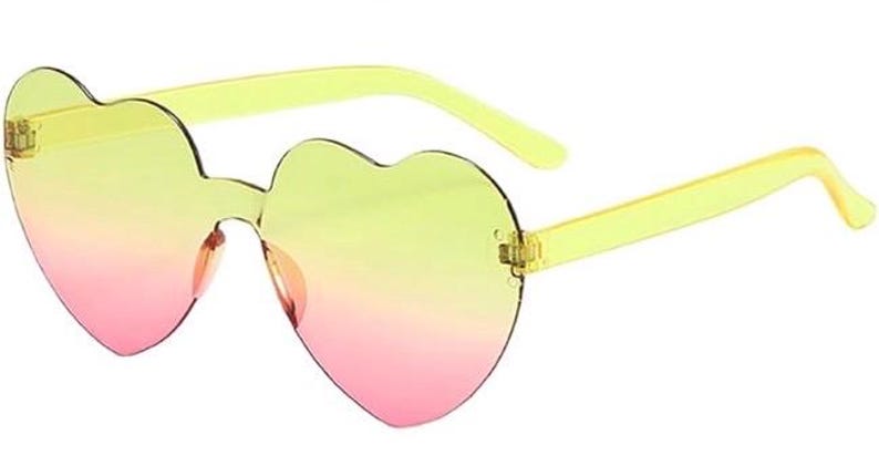 May include: Heart-shaped sunglasses featuring a rimless design with a gradient lens transition from yellow at the top to pink at the bottom. The frames include translucent yellow plastic temples and a matching yellow bridge connecting the lenses.