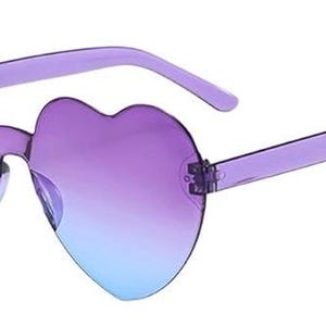May include: Heart-shaped sunglasses featuring a translucent purple frame and gradient lenses that transition from a deep purple at the top to a light blue at the bottom. The rimless design highlights the distinct heart silhouette of the lenses.