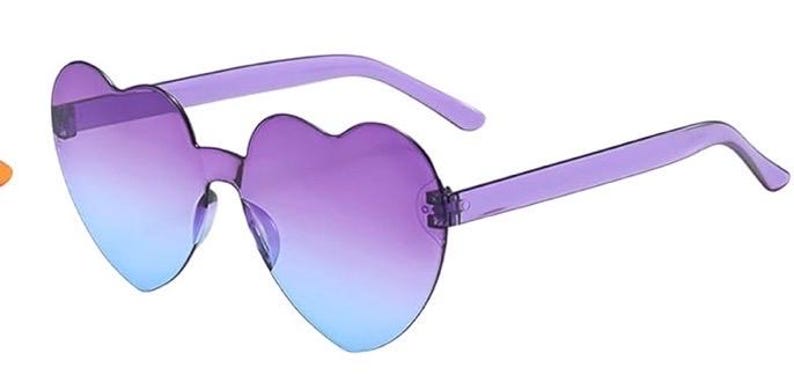 May include: Heart-shaped sunglasses featuring a translucent purple frame and gradient lenses that transition from a deep purple at the top to a light blue at the bottom. The rimless design highlights the distinct heart silhouette of the lenses.