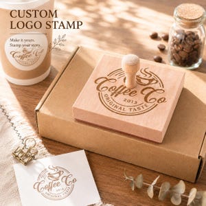 Pode incluir: &Eacute; exibido um carimbo de logotipo personalizado de madeira com o texto "Coffee Co Original Taste 2013". O carimbo est&aacute; ao lado de uma caixa de papel&atilde;o, uma x&iacute;cara de caf&eacute; e um pequeno pote de gr&atilde;os de caf&eacute;. As palavras "Custom Logo Stamp" est&atilde;o no topo.