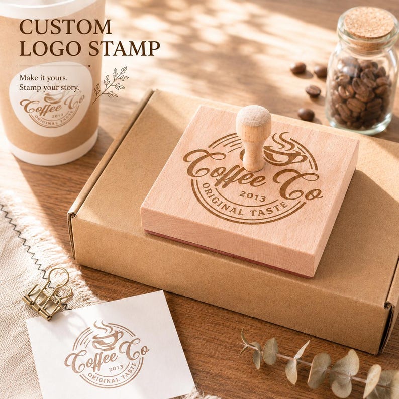 Pode incluir: &Eacute; exibido um carimbo de logotipo personalizado de madeira com o texto "Coffee Co Original Taste 2013". O carimbo est&aacute; ao lado de uma caixa de papel&atilde;o, uma x&iacute;cara de caf&eacute; e um pequeno pote de gr&atilde;os de caf&eacute;. As palavras "Custom Logo Stamp" est&atilde;o no topo.