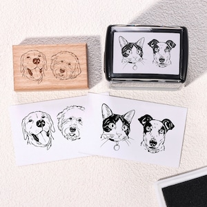 May include: A set of four custom pet portrait stamps. The stamps are made of wood and feature black and white illustrations of a cat, a labrador retriever, and two other dogs. The stamps are arranged in a grid pattern on a white background.