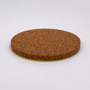 May include: A round cork coaster with a gold trim. The coaster is made of natural cork and has a rough texture.