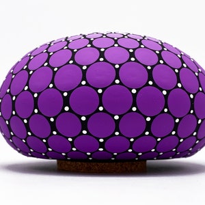 May include: A purple ceramic egg with a black and white polka dot pattern. The egg is sitting on a cork base.